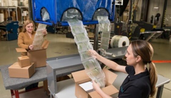 Warehouse worker using an automated air pillow machine to pack boxes that will be shipped out for delivery.